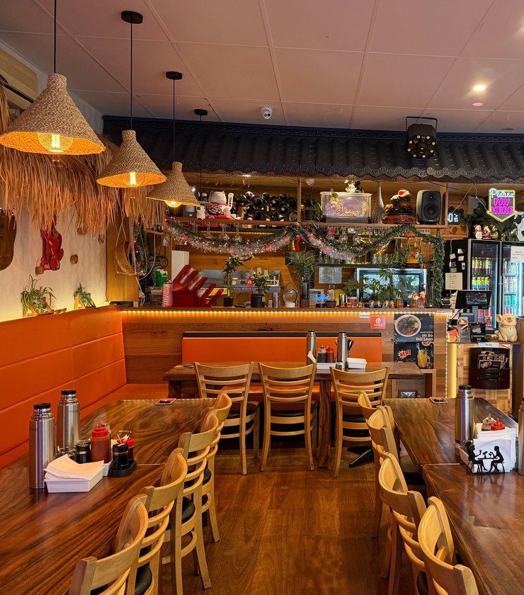 The Athol Road dining room: thatched pendant lights over live-edge timber tables and orange banquette seating