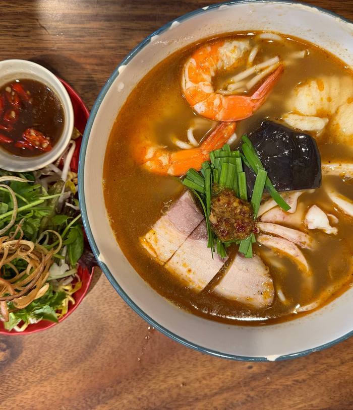 A bowl of bún mắm beside a plate of herbs