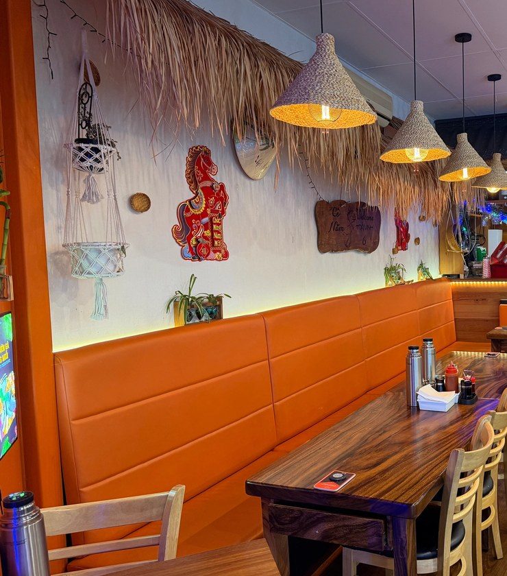 A feature wall of dried palm fronds, macramé planters and a carved Cô Năm Trà Vinh welcome board above the banquette