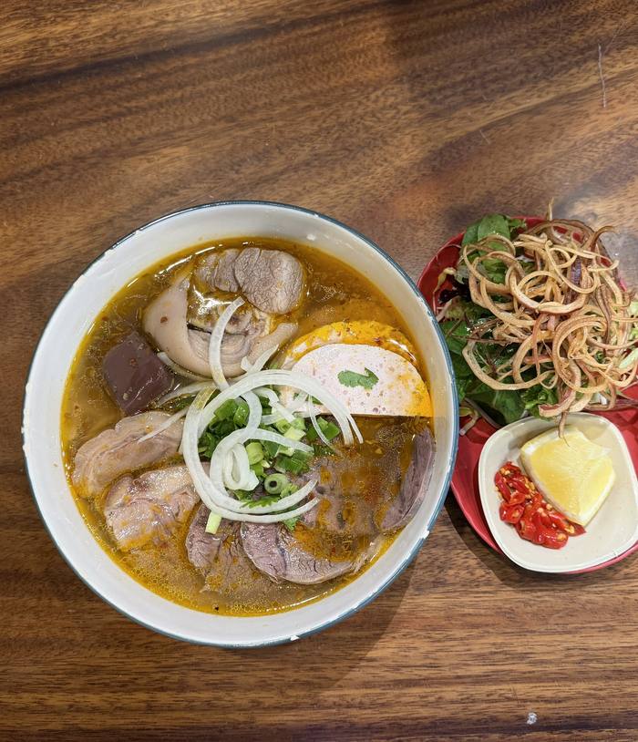 A bowl of bún bò Huế beside a plate of herbs