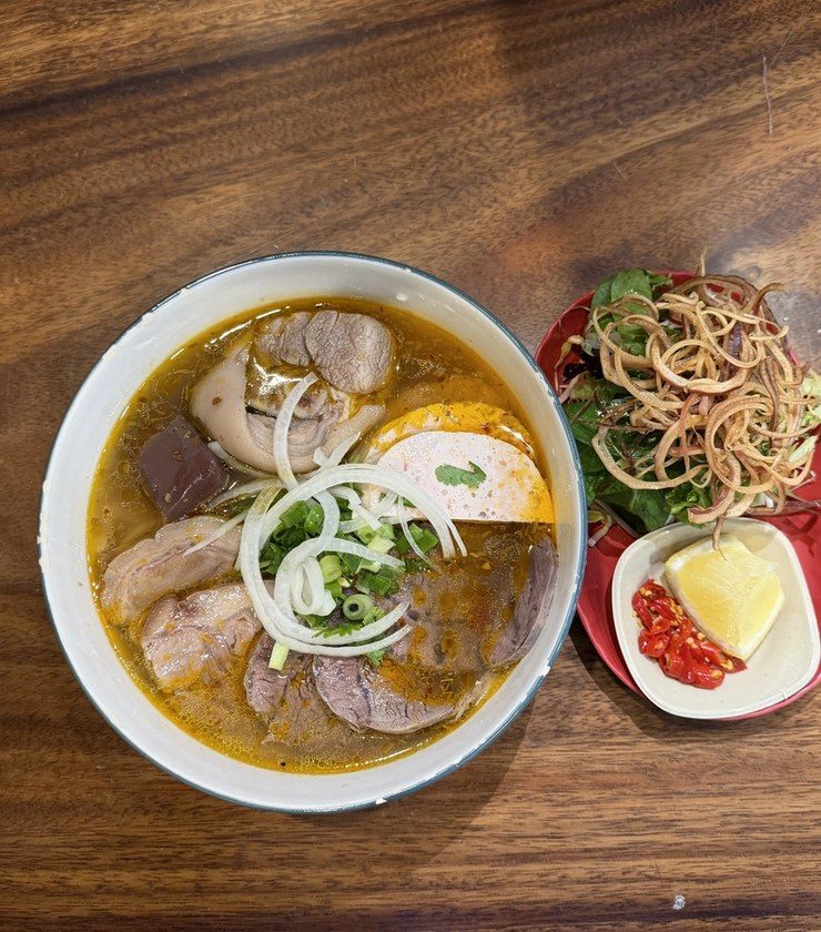 A bowl of bún bò Huế, the spicy lemongrass beef noodle soup, with sliced pork, pork loaf and spring onion