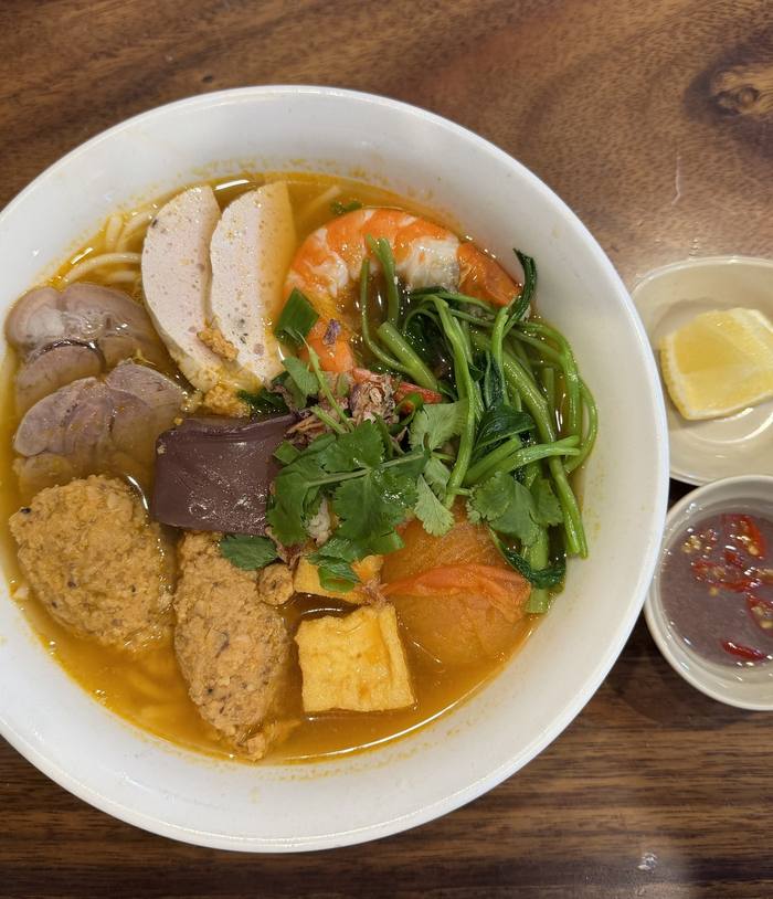 A bowl of bún riêu beside a lemon wedge and a dipping sauce