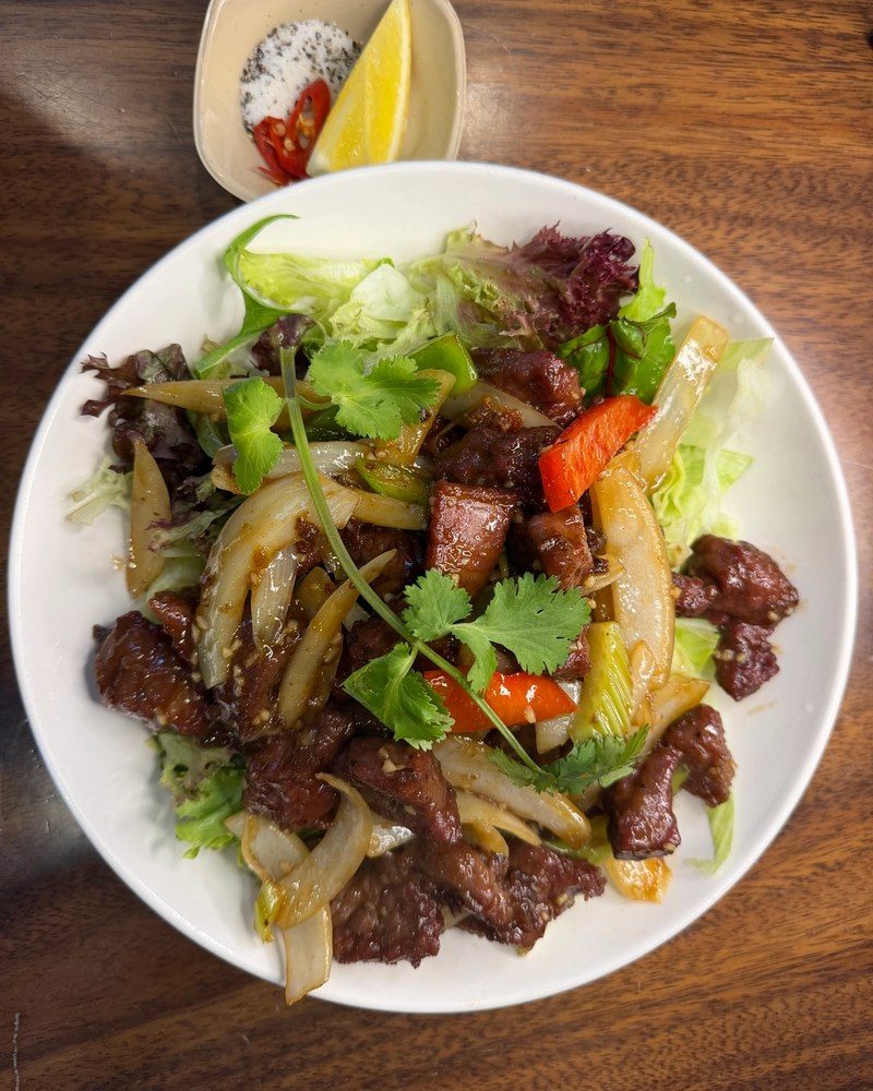 Diced beef stir-fried with onion and capsicum on salad leaves, with a salt, pepper and lemon dip