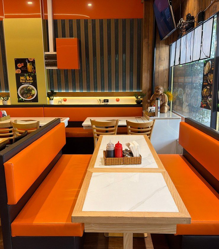 A window booth at Windsor Avenue, orange banquettes and a marble-top table beside the street glass